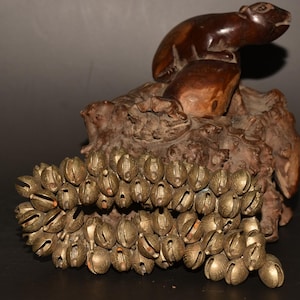 Op de afbeelding: Een houten beeldje van een knaagdier dat op een boomstronk zit met een ketting van messingbellen die eronder hangen.