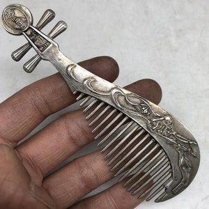 May include: A silver comb shaped like a Chinese pipa, a traditional musical instrument. The comb features intricate details and a decorative design.