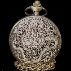 May include: A gold-toned pocket watch with a detailed dragon design on the face. The watch has a chain attached to it.