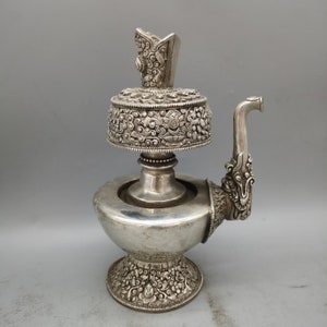 May include: A silver-coloured metal teapot with intricate floral designs and a dragon-shaped spout. The teapot has a removable top with a small finial.