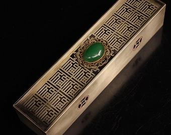 Op de afbeelding: Een rechthoekige messing wierookbrander met een ingewikkeld geometrisch ontwerp. De brander heeft een groene jade-steen die is gezet in een decoratief metalen frame.