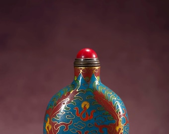 May include: A small, ornate, blue, red, and gold cloisonné bottle with a red stopper. The bottle features a detailed design of dragons and clouds. The bottle is likely a decorative item or a container for perfume or other liquids.