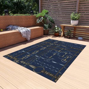 May include: A rectangular navy blue rug with a repeating pattern of equestrian bits and chains in gold and silver. The rug is placed on a wooden deck, with outdoor furniture and plants in the background.