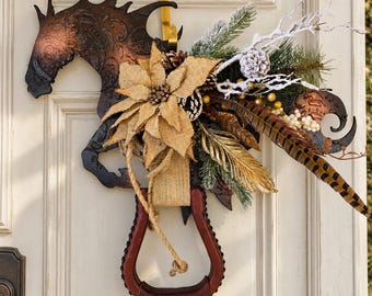Può includere: Una decorazione da parete con una sagoma di cavallo in metallo marrone scuro decorata con una stella di Natale in iuta, rami di pino, bacche bianche e piume di fagiano, appesa a un gancio dorato sopra una staffa in cuoio marrone.