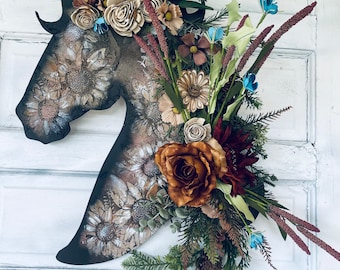 Può includere: Una silhouette di cavallo nero con una ghirlanda floreale fatta di fiori marroni, bianchi e blu. La ghirlanda comprende fiori marroni, bianchi e blu, foglie verdi e rami marroni.