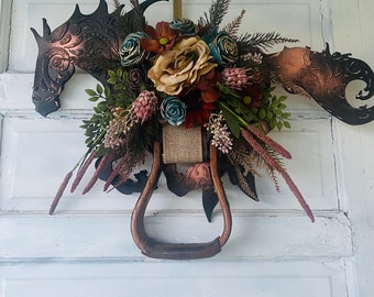 Può includere: Una ghirlanda rustica a forma di testa di cavallo con uno stivale in cuoio marrone e una varietà di fiori autunnali, tra cui il bordeaux, la ruggine e la crema.