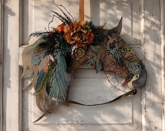 Può includere: Una decorazione da parete in metallo a forma di testa di cavallo con un design intagliato e intricati motivi floreali. La criniera è decorata con un gruppo di fiori artificiali arancioni e marroni, piante grasse verdi e fogliame scuro.