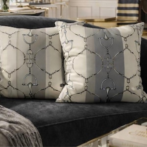 May include: Two decorative throw pillows with a horse bit pattern in gray and white stripes. The pillows are on a dark gray sofa, creating a sophisticated and elegant look. The pillows add a touch of equestrian style to the room.