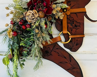 Puede incluir: Una corona de cabeza de caballo de cuero marrón decorada con acentos florales rojos, dorados y verdes. La corona está adornada con bayas y vegetación, creando un aspecto navideño festivo.