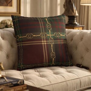 May include: A decorative square pillow with a plaid pattern in burgundy, green, and gold. The pillow features a gold chain design and is placed on a beige tufted sofa. The scene suggests a classic, elegant interior.