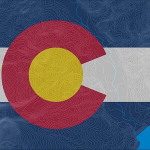 Pode incluir: Um mapa topográfico estilizado da bandeira do estado do Colorado. A bandeira apresenta um círculo vermelho grande com um círculo amarelo menor dentro. A palavra "PROOF" está escrita em texto verde no canto superior esquerdo da bandeira.