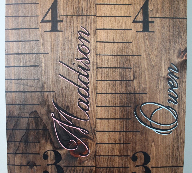 May include: A wooden growth chart with black numbers and lines. The names "Madison" and "Owen" are written in cursive on the chart, with "Madison" in pink and "Owen" in blue.
