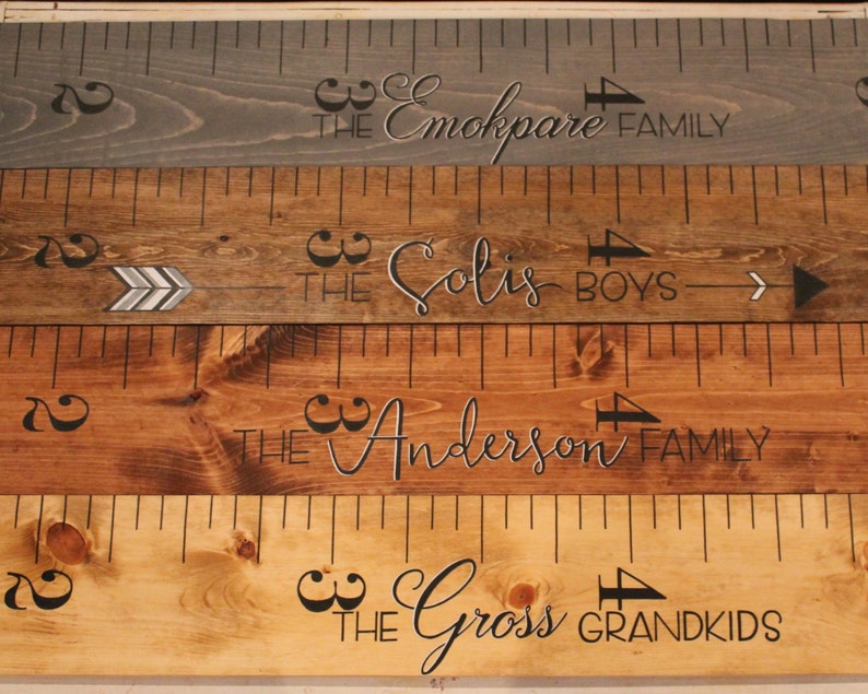 May include: Four wooden growth charts with black markings and arrows. The top chart reads "The Emokpare Family". The second chart reads "The Solis Boys". The third chart reads "The Anderson Family". The bottom chart reads "The Gross Grandkids".