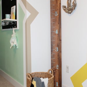 May include: A wooden growth chart with blue numbers from 1 to 6, a wicker basket with a blanket inside, and a driftwood anchor on the wall.