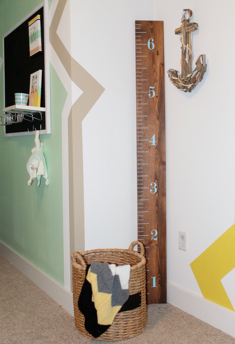 May include: A wooden growth chart with blue numbers from 1 to 6, a wicker basket with a blanket inside, and a driftwood anchor on the wall.