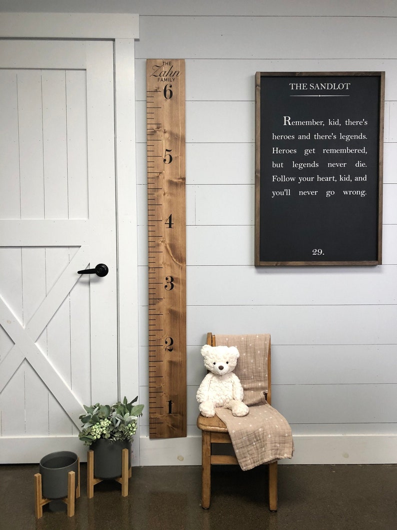 May include: A wooden growth chart with the text "The Zahn Family" and numbers 1 through 6. A black chalkboard sign with the text "The Sandlot" and a quote from the movie. A teddy bear sits on a wooden chair with a white and brown blanket.