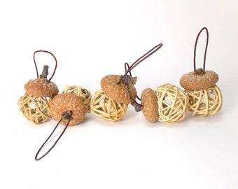 Può includere: Una catena di sei ornamenti a forma di ghianda con gabbie di filo metallico intrecciato. Le ghiande sono marroni e le gabbie sono beige.