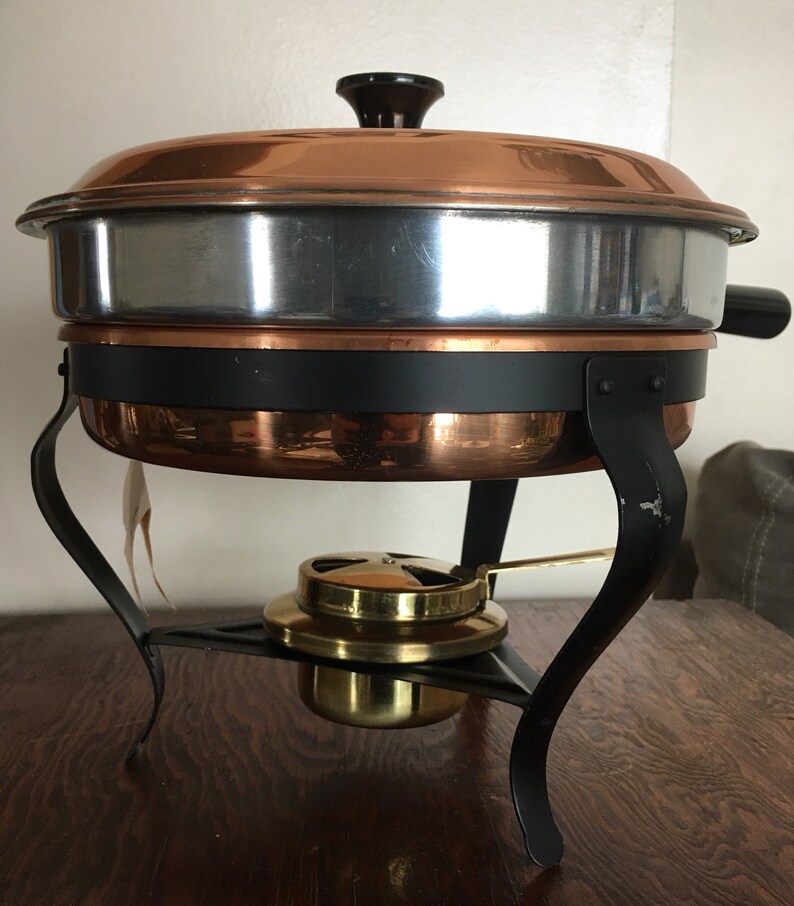 May include: A copper chafing dish with a black stand and a brass burner. The chafing dish has a silver lining and a black knob on the lid.