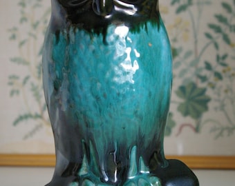 May include: A ceramic owl figurine with a teal and black glaze. The owl is perched on a branch with its wings spread out.