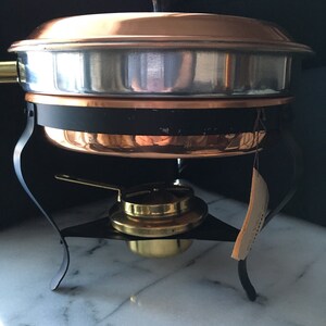 May include: A copper chafing dish with a black stand and a brass burner. The chafing dish has a silver lining and a lid with a black knob.