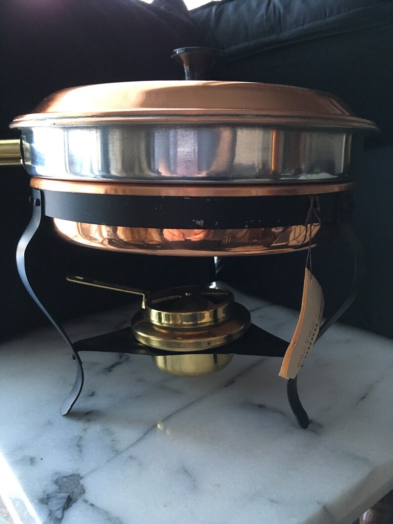 May include: A copper chafing dish with a black stand and a brass burner. The chafing dish has a silver lining and a lid with a black knob.