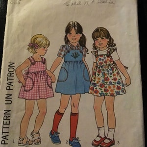May include: Simplicity pattern 8043 for a child's dress. The pattern shows illustrations of three girls in various dresses. The pattern includes the text "ONE PATTERN UN PATRON" and "SIZE 6 CHILD".