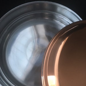 May include: A stainless steel pot with a copper lid. The pot has a shiny, reflective surface.
