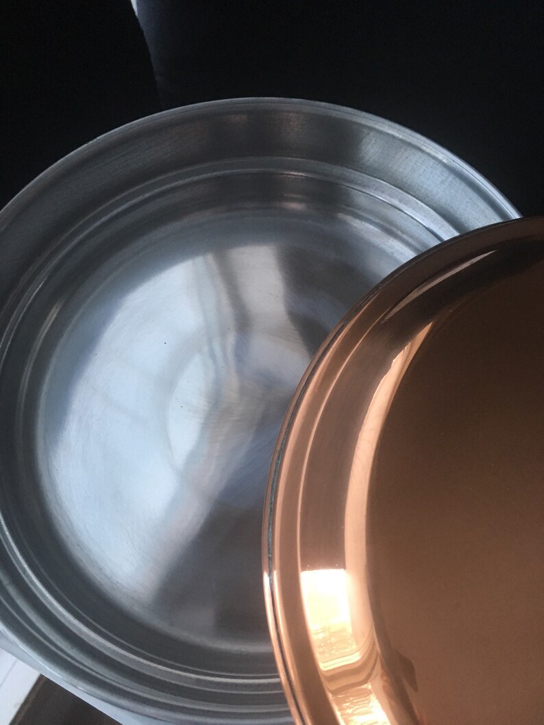 May include: A stainless steel pot with a copper lid. The pot has a shiny, reflective surface.