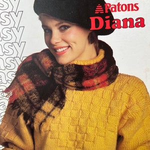 May include: A woman wearing a black beret, a plaid scarf, and a yellow sweater with a textured, square pattern. The image includes the text "Beehive Shetland-Style Chunky" and "Patons Diana".