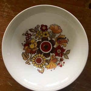 May include: A white ceramic bowl featuring a floral design in shades of red, orange, yellow, and brown. The flowers are stylised and have a retro look.
