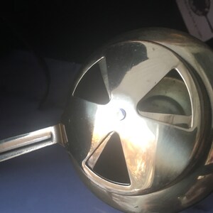 May include: A gold-colored metal hookah bowl with a handle and four holes on the top. The bowl is designed to hold shisha tobacco and charcoal.