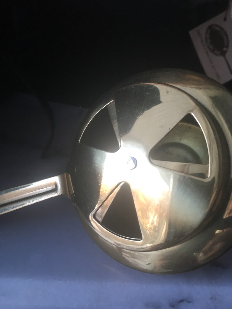 May include: A gold-colored metal hookah bowl with a handle and four holes on the top. The bowl is designed to hold shisha tobacco and charcoal.