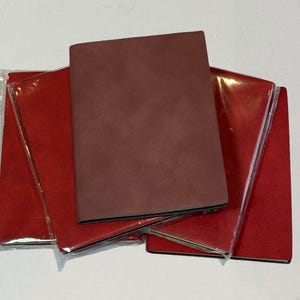 Puede incluir: Un conjunto de cuadernos. Uno es de color marrón oscuro, y los otros son rojos. Algunos de los cuadernos rojos están en envases de plástico transparente. Los cuadernos son rectangulares y parecen estar hechos de un material texturizado.