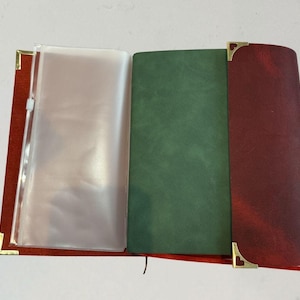 Puede incluir: Diario de cuero abierto con una cubierta roja, p&aacute;ginas interiores verdes y burdeos y una funda de pl&aacute;stico transparente. Las esquinas doradas a&ntilde;aden un toque decorativo. El diario est&aacute; abierto, mostrando las p&aacute;ginas interiores.