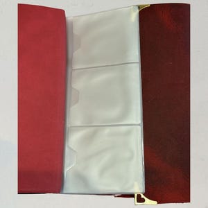 Puede incluir: &Aacute;lbum de fotos abierto con lomo rojo y cubierta burdeos. El &aacute;lbum tiene fundas de pl&aacute;stico transparente para guardar fotos. Las esquinas doradas a&ntilde;aden un toque decorativo.