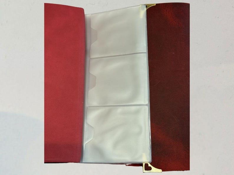 Puede incluir: &Aacute;lbum de fotos abierto con lomo rojo y cubierta burdeos. El &aacute;lbum tiene fundas de pl&aacute;stico transparente para guardar fotos. Las esquinas doradas a&ntilde;aden un toque decorativo.