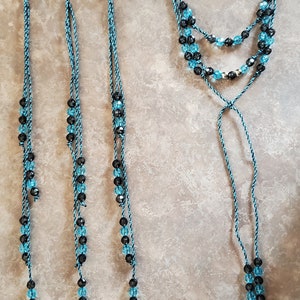 May include: Four strands of black and turquoise beaded cord with silver clips at the top. The cords are tied together at the bottom to form a necklace.