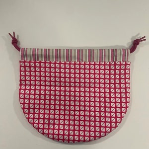 Puede incluir: Una bolsa de cord&oacute;n rosa y blanca con un patr&oacute;n geom&eacute;trico. La bolsa tiene un ribete de rayas blancas y rosas alrededor de la parte superior.