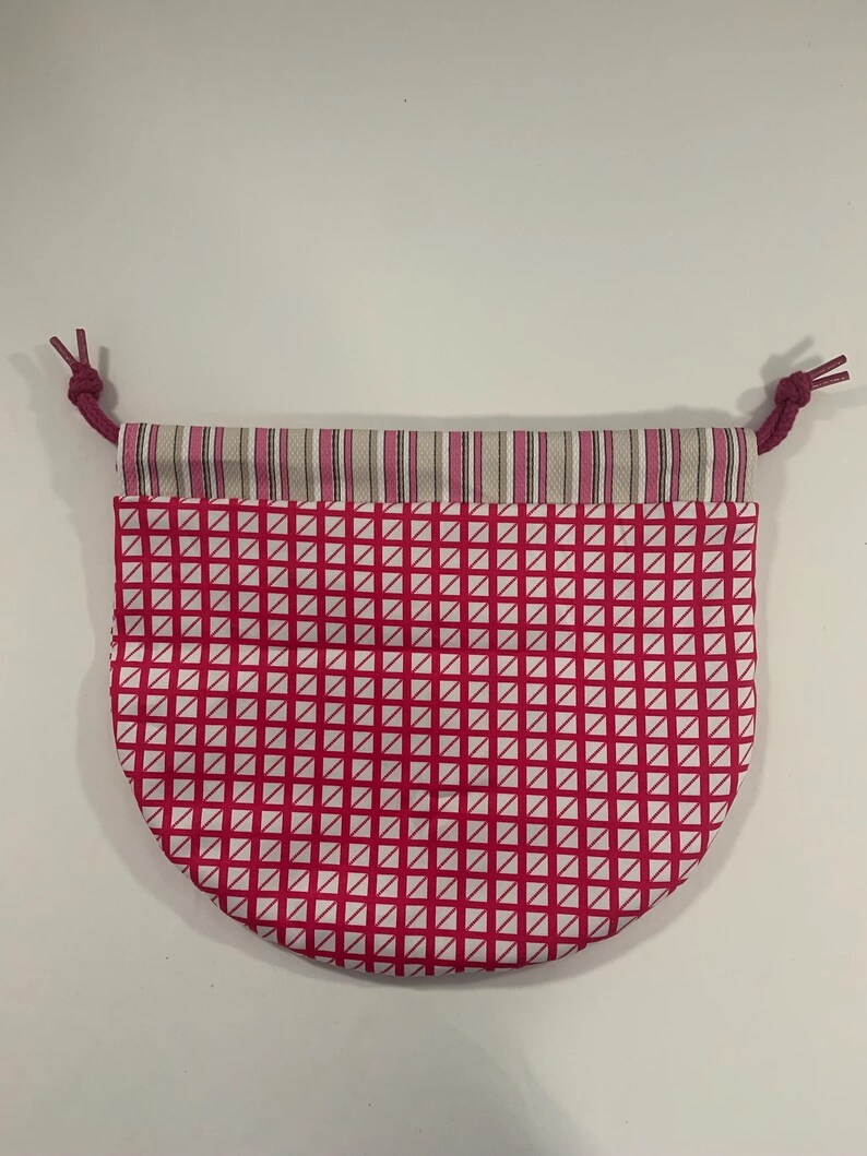 Puede incluir: Una bolsa de cord&oacute;n rosa y blanca con un patr&oacute;n geom&eacute;trico. La bolsa tiene un ribete de rayas blancas y rosas alrededor de la parte superior.