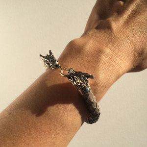 May include: A silver bracelet with two dragon heads at the ends. The bracelet is made of textured metal that resembles scales.