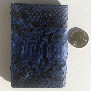 May include: A small, dark blue leather wallet with a snakeskin pattern. The wallet is about the size of a US quarter.
