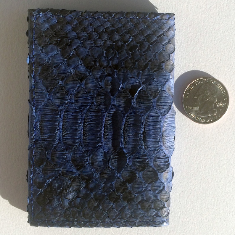 May include: A small, dark blue leather wallet with a snakeskin pattern. The wallet is about the size of a US quarter.