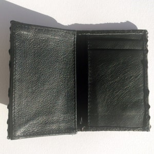 May include: A black leather wallet with a textured exterior and a single interior pocket. The wallet is folded open to reveal the interior.