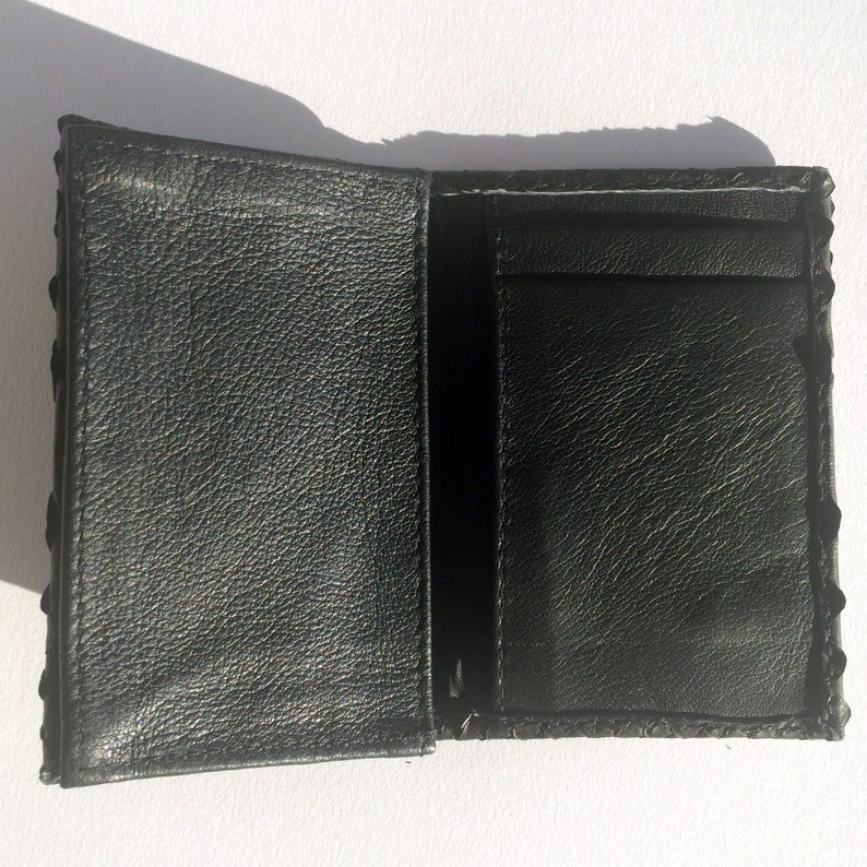 May include: A black leather wallet with a textured exterior and a single interior pocket. The wallet is folded open to reveal the interior.