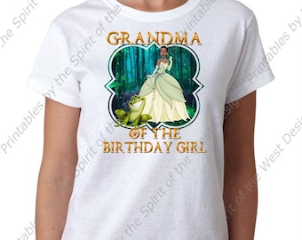May include: White t-shirt with a graphic of a princess and a frog in a forest setting. The text "Grandma of the Birthday Girl" is printed on the shirt.