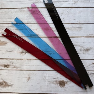 May include: Four colorful, transparent rulers in red, blue, pink, and black, arranged diagonally on a light wood surface. Each ruler has a notched end and text that reads "Waterfall Threads 36" Loop Measurement Tool."