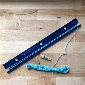 May include: A blue Waterfall Threads Floss measurement tool with light blue thread. The tool has the text "Waterfall Threads Floss Measurement Tool". A small label with a barcode is also present.