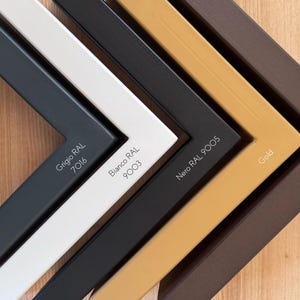 May include: Close-up of five picture frame corners in various colors: gray (Grigio RAL 7016), white (Bianco RAL 9003), black (Nero RAL 9005), gold, and brown (Effetto Corten). Each corner displays its color name and RAL code in white text.