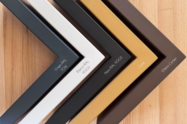 May include: Close-up of five picture frame corners in various colors: gray (Grigio RAL 7016), white (Bianco RAL 9003), black (Nero RAL 9005), gold, and brown (Effetto Corten). Each corner displays its color name and RAL code in white text.