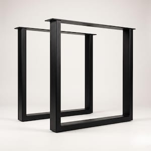 Könnte beinhalten: Ein Paar schwarze Tischbeine aus Metall mit rechteckigem Rahmendesign. Jedes Bein verfügt über eine flache Montageplatte mit vorgebohrten Löchern, die mit zwei vertikalen Pfosten und einer horizontalen Basisstange zu einer U-Form verbunden ist.